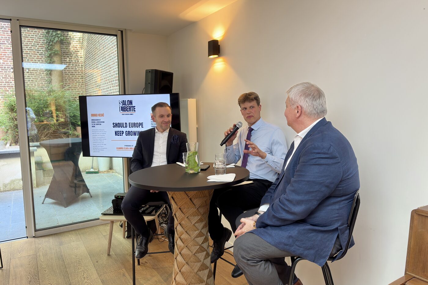 Three panellists at a high table, one speaking into a microphone