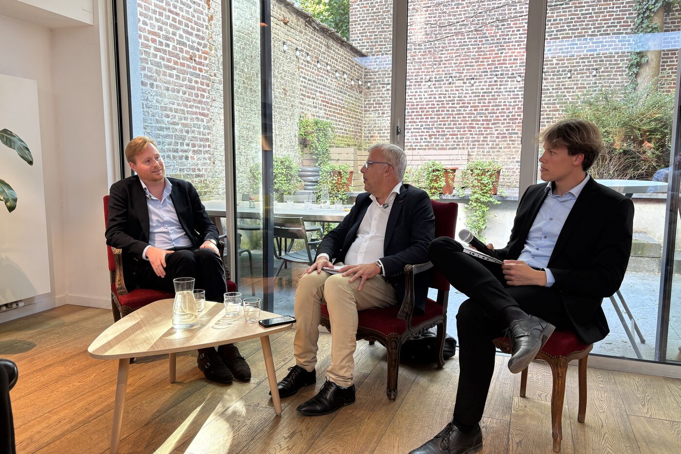 Three panellists in armchairs around a low table in a sunlit room